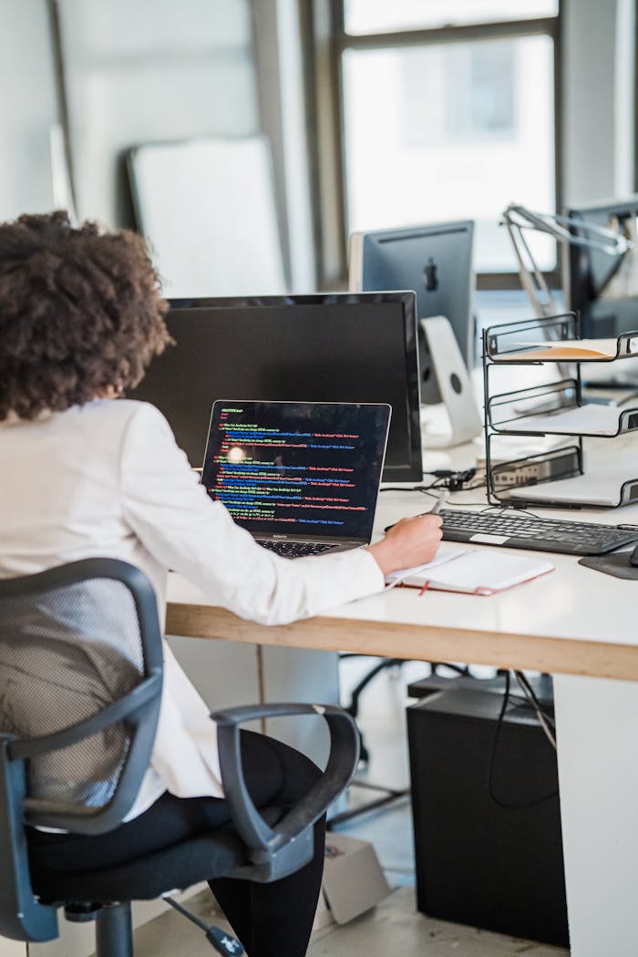 Focused businesswoman coding at desk in a modern office setting, showcasing concentration and technology skills.